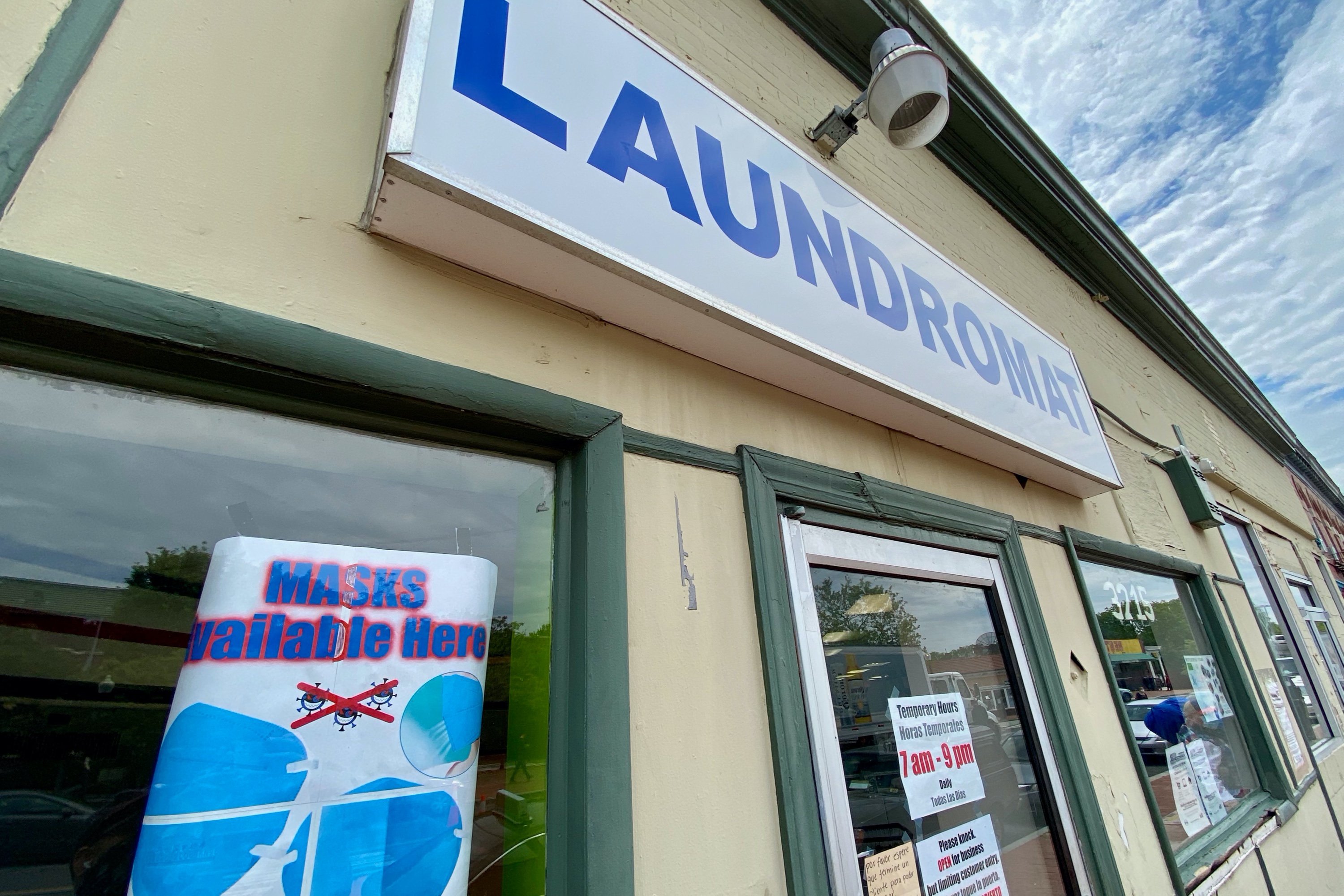Exterior shot of a laundromat with a sign in the window: "Masks available here"