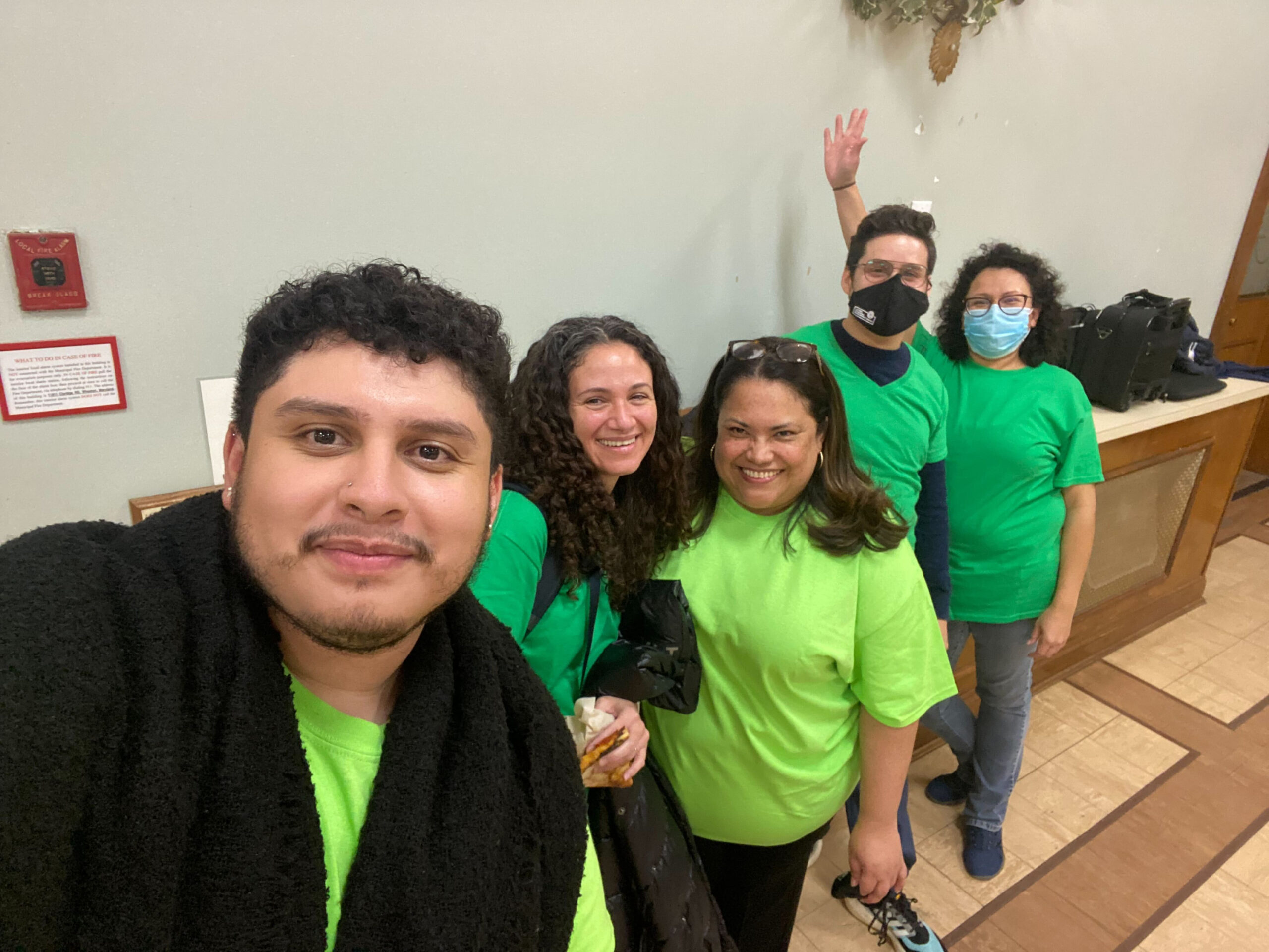 Photo showing five people posing for a photo, all wearing similarly colored shirts.