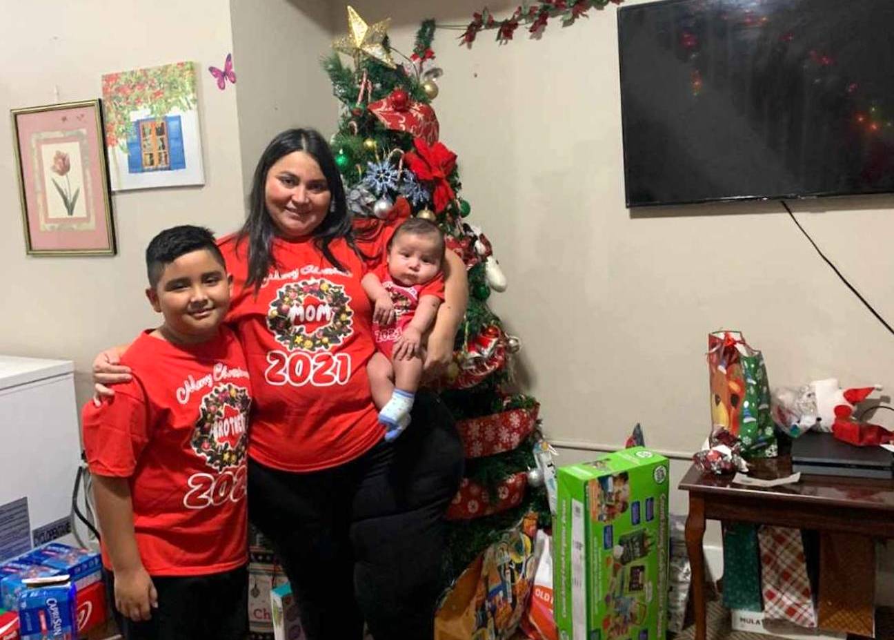 Photo of a woman and her two children posing in front of a Christmas tree, all wearing matching holiday t-shirts.