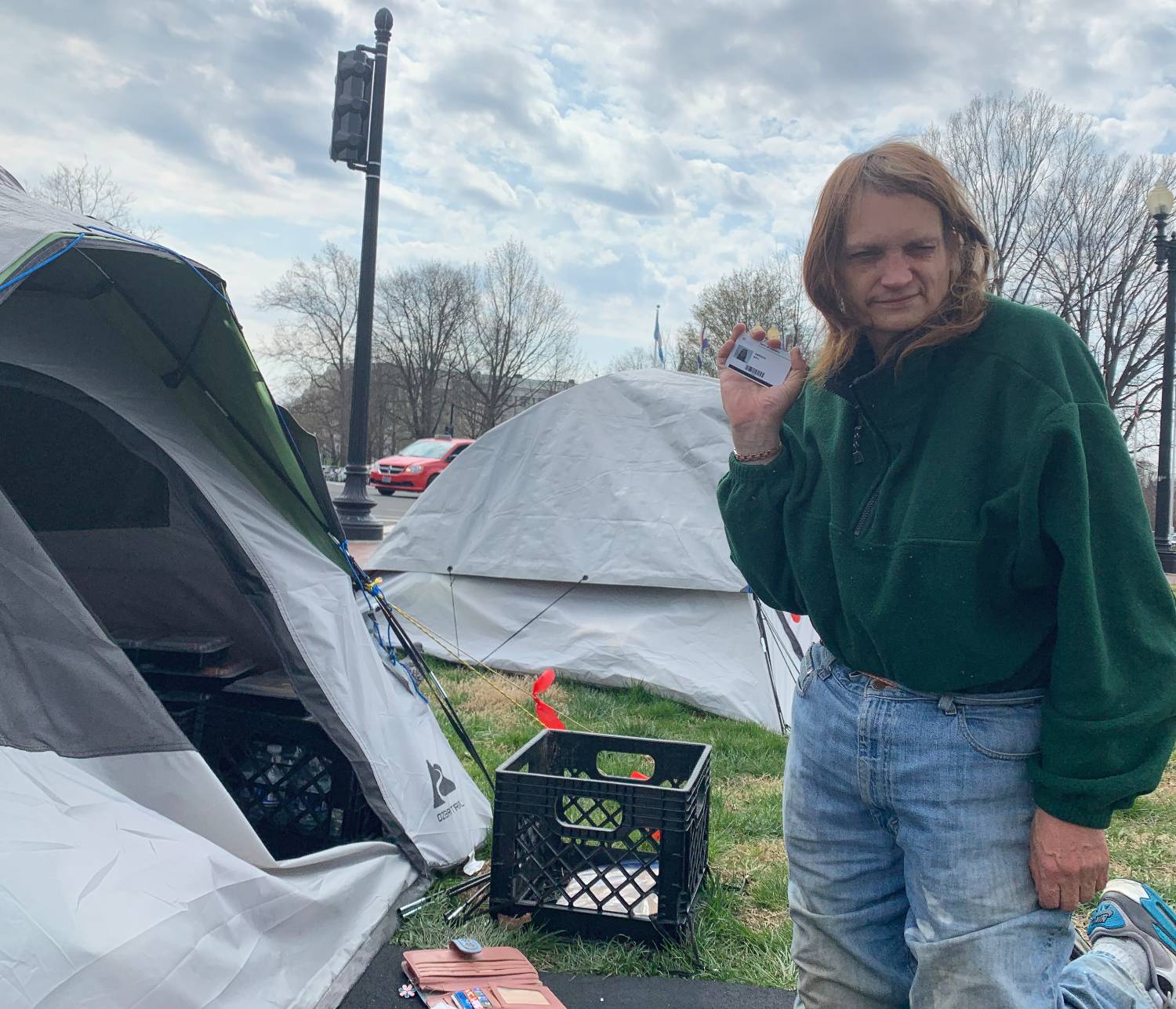 Photo of a person standing amid several tents on a grass lawn with cars in the background.