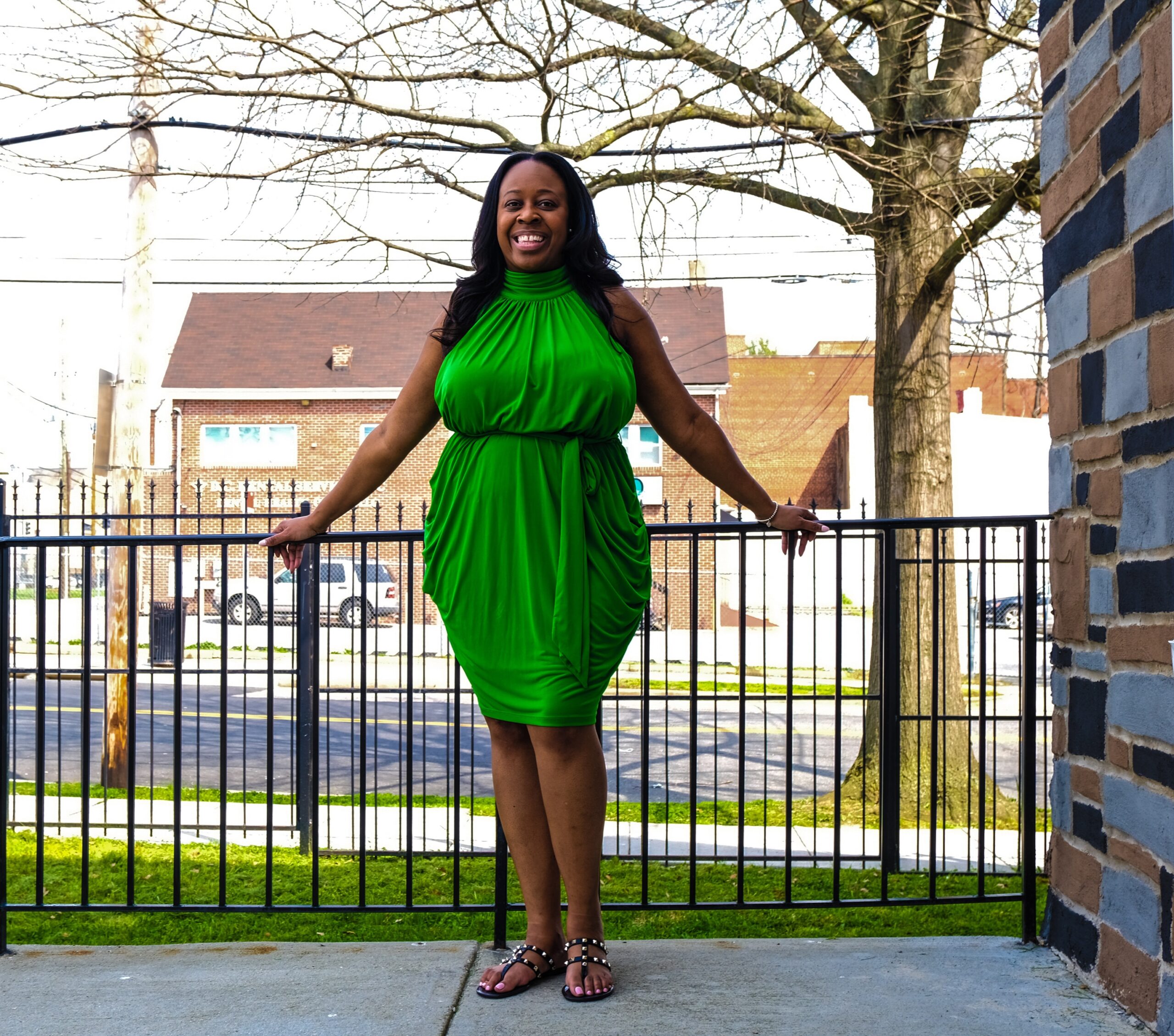 Photo of a woman in a green dress standing outside on a porch and smiling.