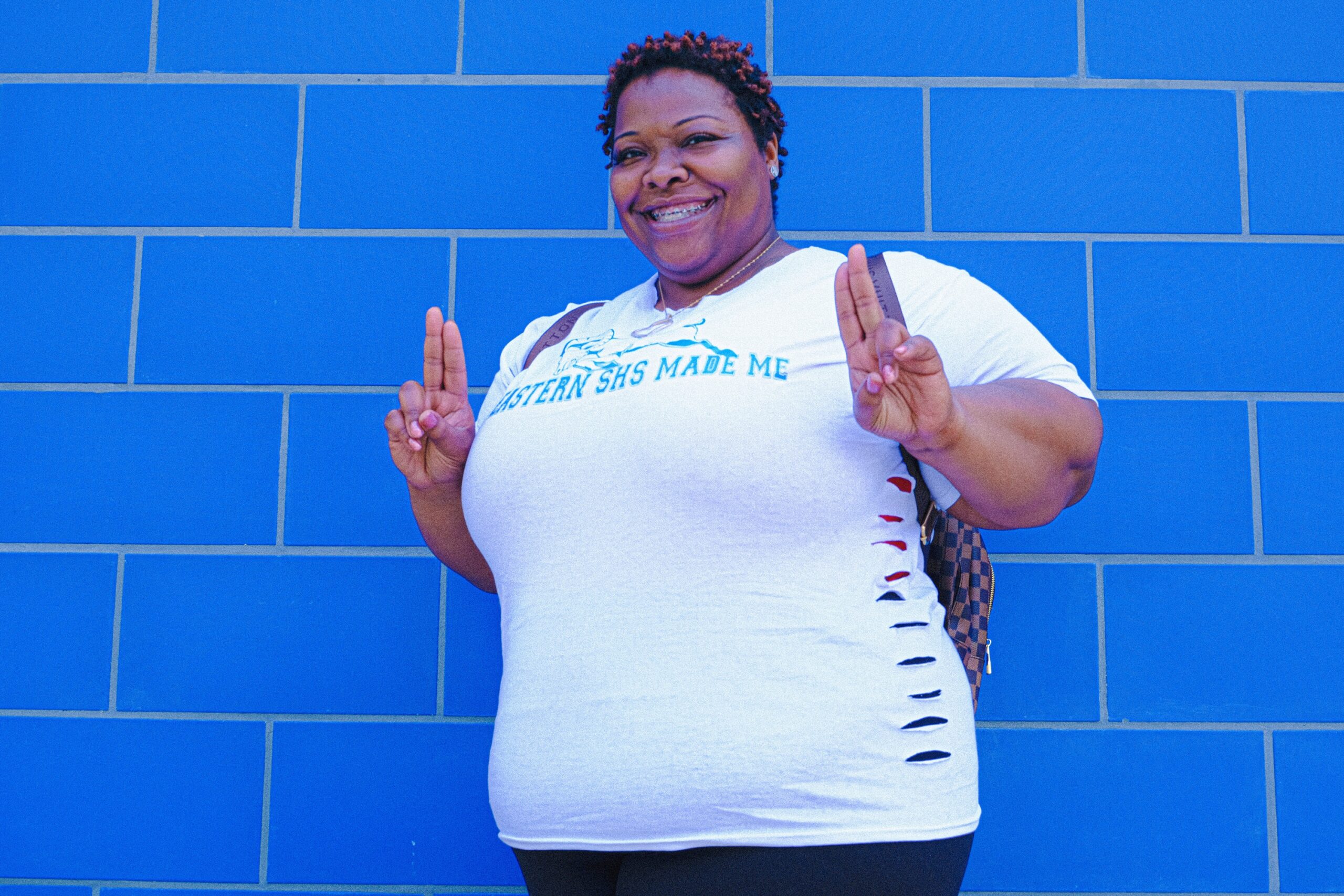 Photo of a woman smiling and standing in front of a blue wall.