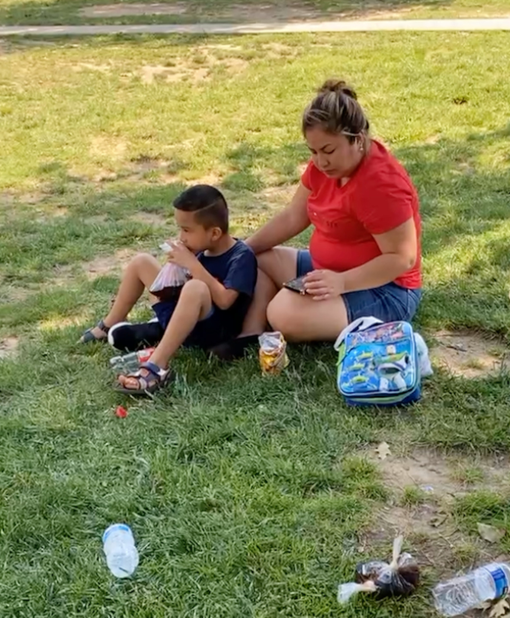Photo of a woman and a young boy sitting together in the middle of a patch of grass in the summer heat.