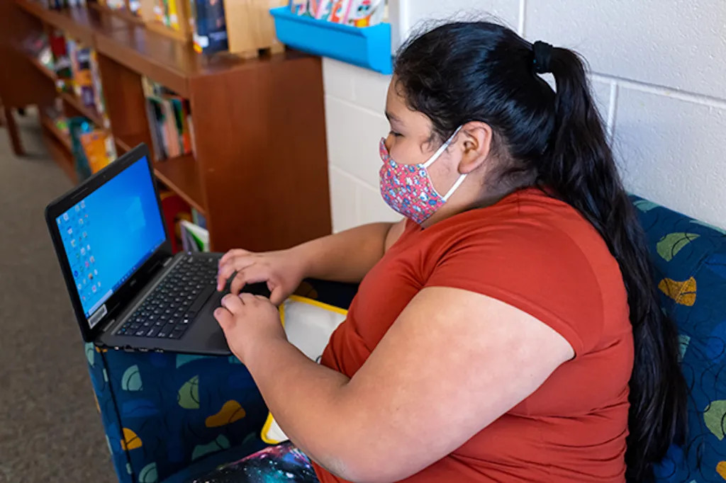 Photo of a woman wearing a face mask to protect against COVID-19 sitting with a laptop