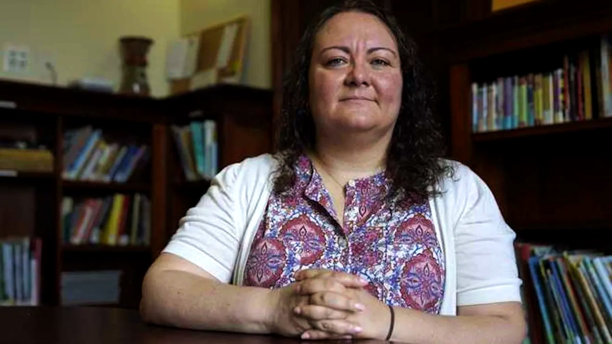 Photo showing LaRue seated at a table indoors with her fingers crossed. Bookshelves are visible behind her.