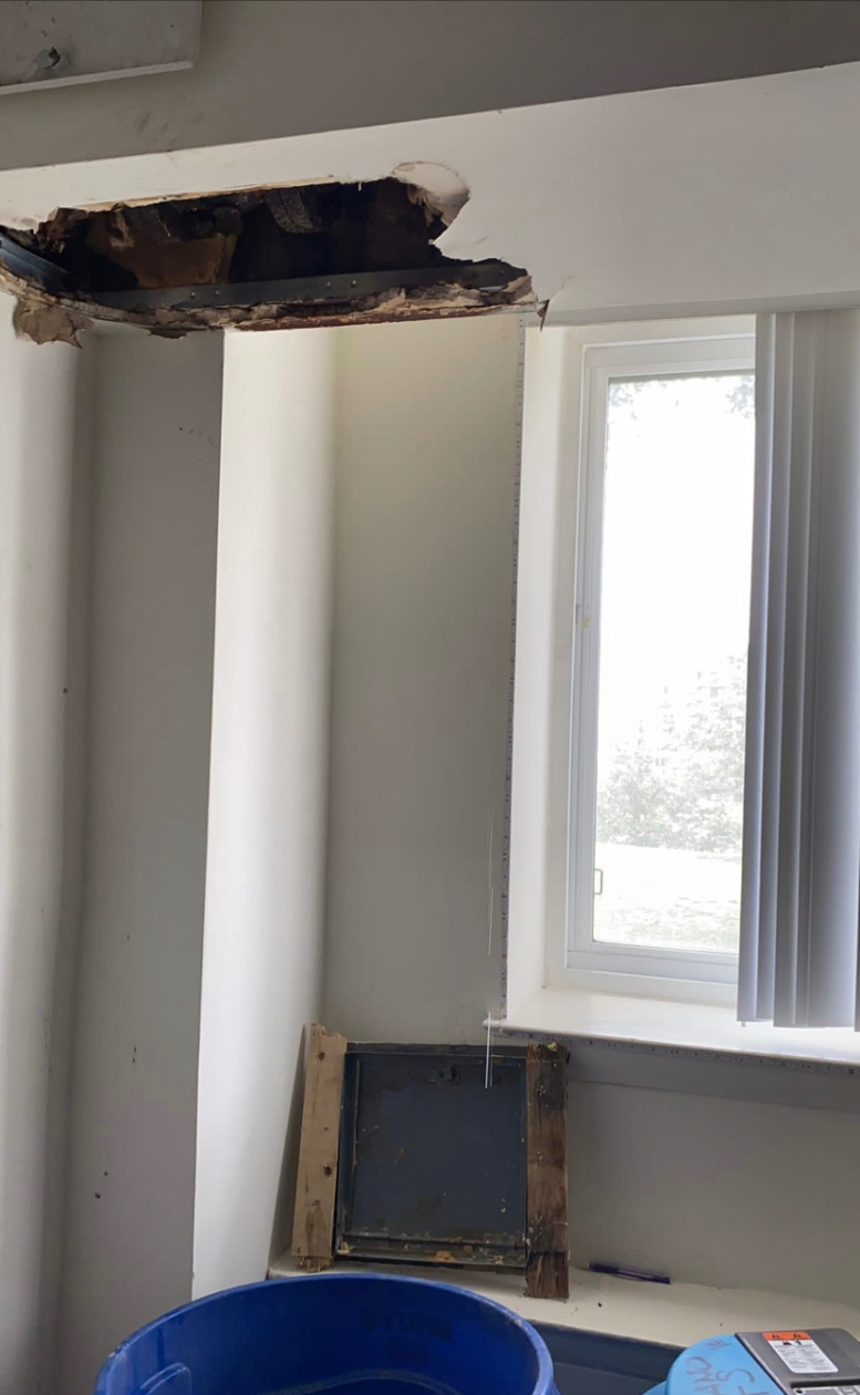 Photo of a 3-4 foot hole in a ceiling near a window.