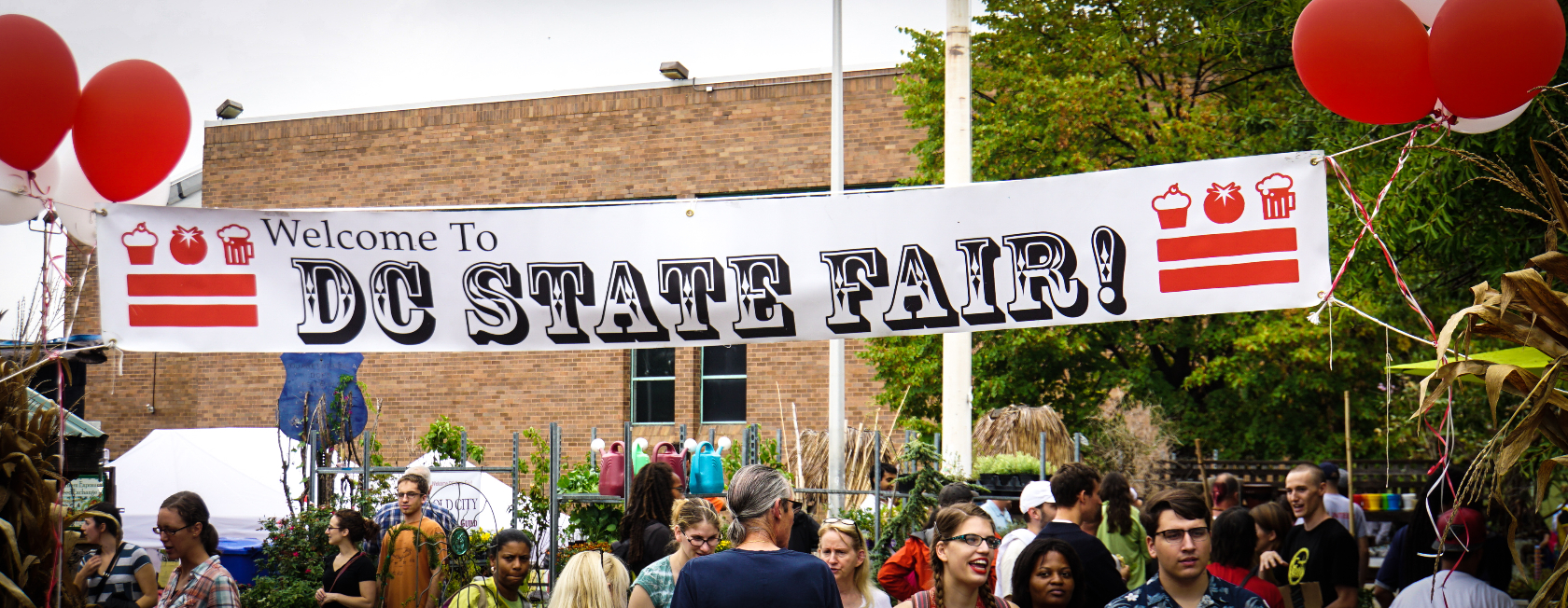 Photo showing a "Welcome to the DC State Fair" banner and a crowd of people under it