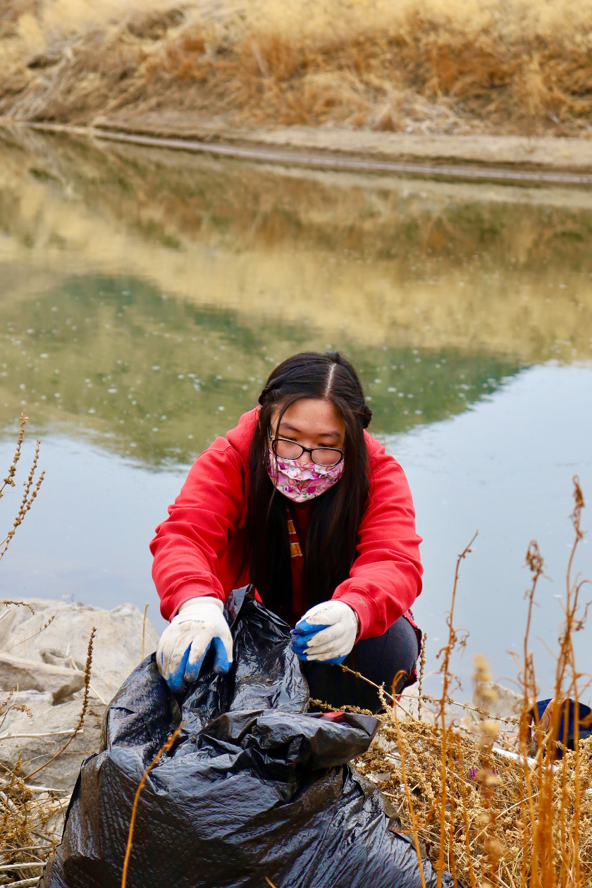 photo of a woman near the edge of water, cleaning up trash
