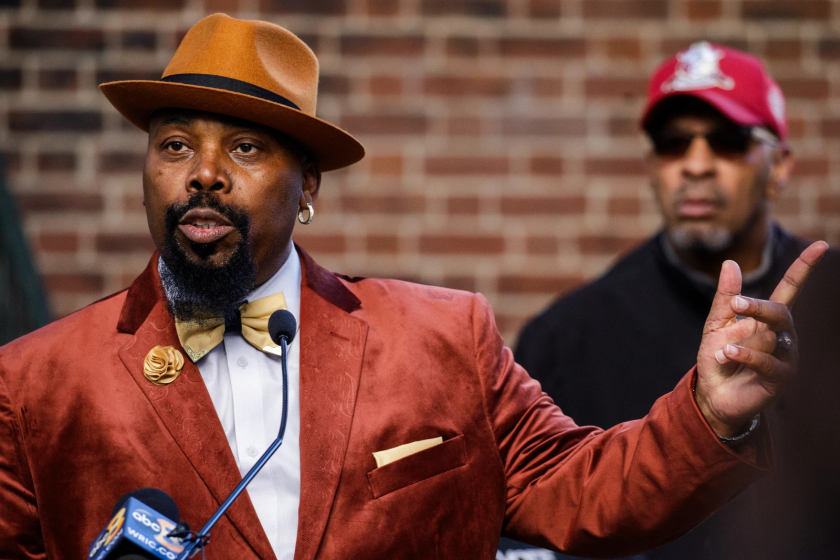 Photo of Hill wearing a suit and speaking into a microphone.