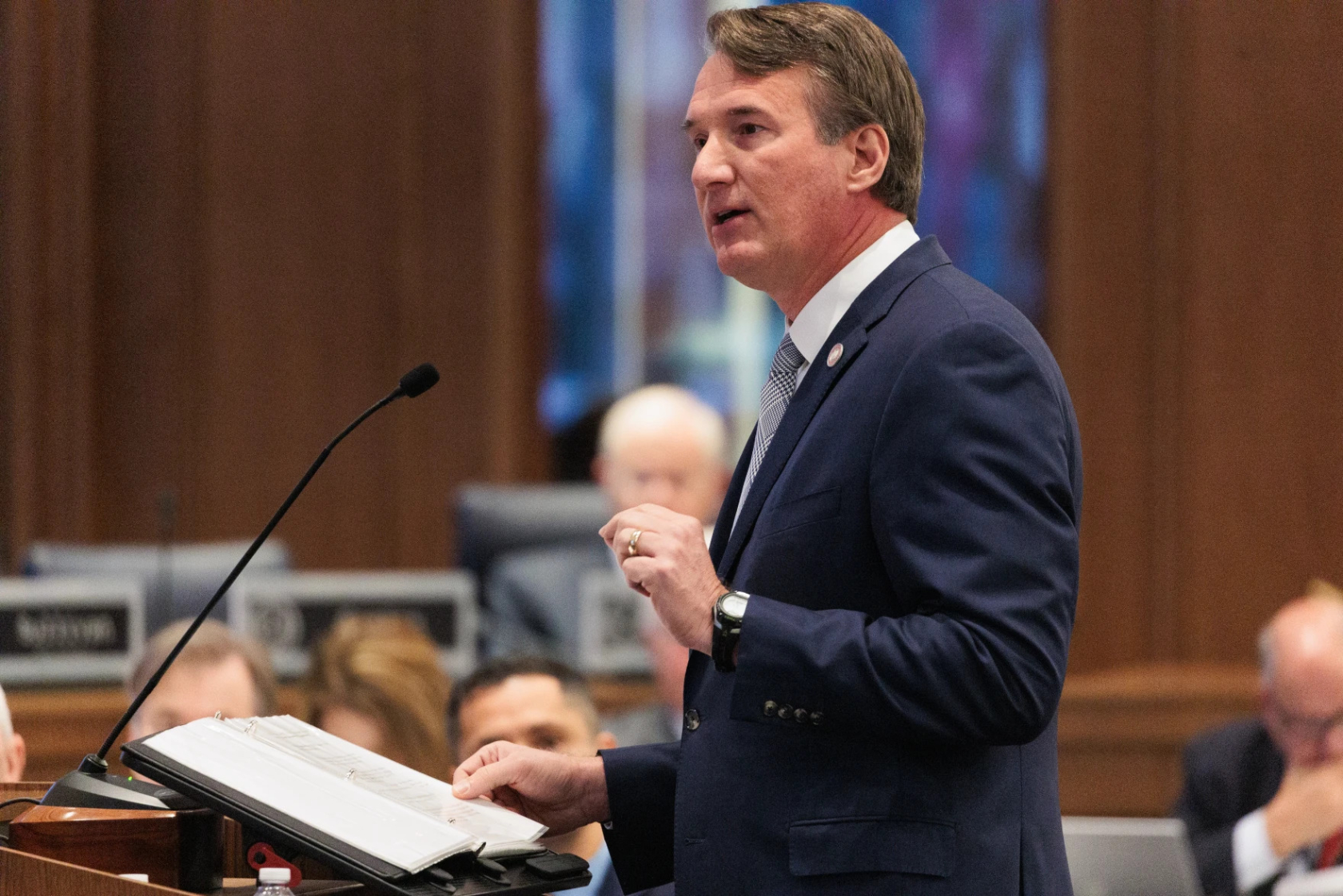 Photo of a man in a suit speaking at a microphone.