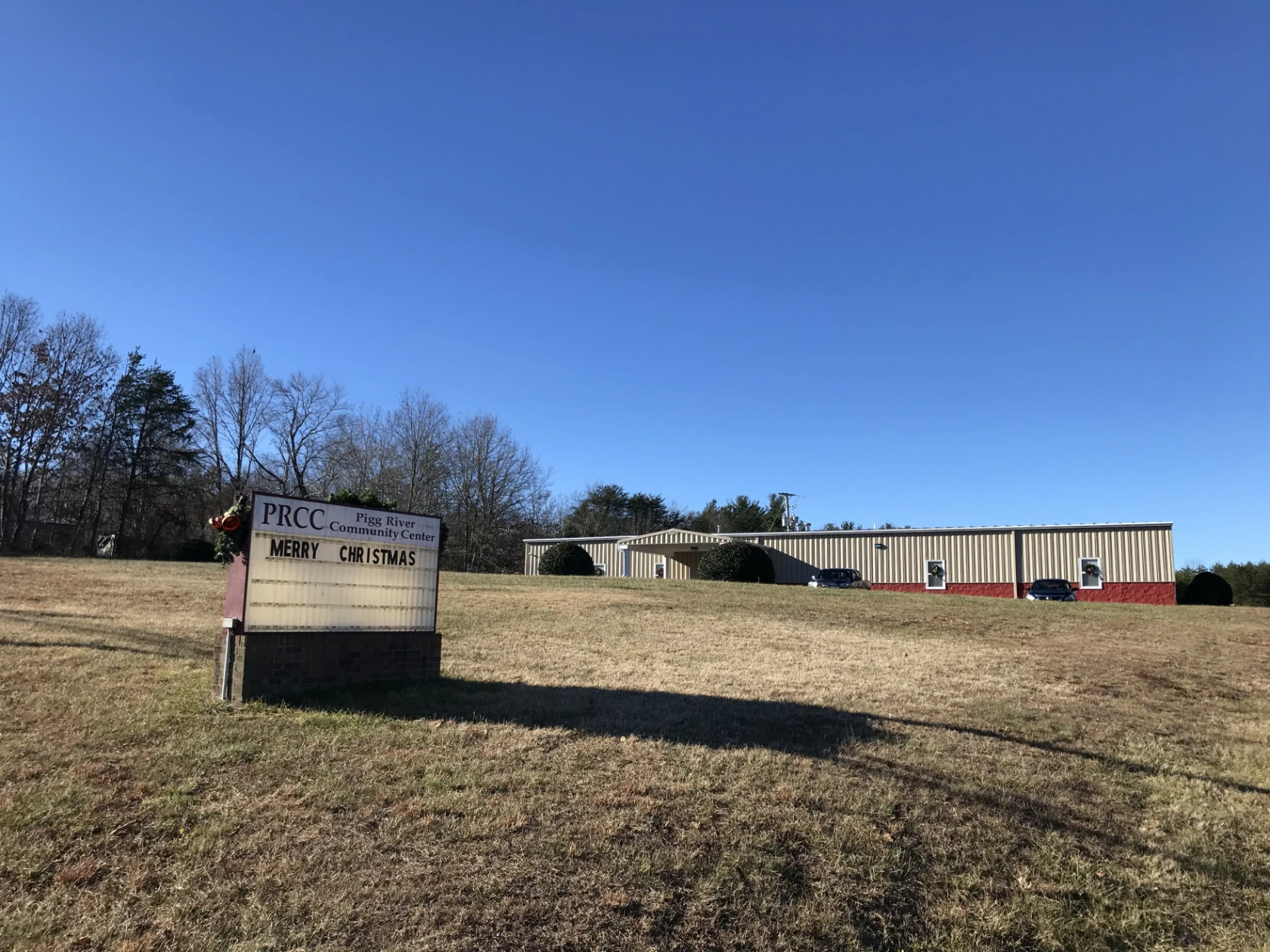 Photo of the community center building at a distance. A sign in the foreground, where the letters/message can be changed, says "Merry Christmas"