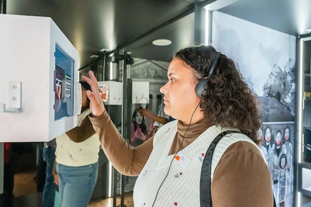 Photo of a student standing in the trailer, wearing headphones and interacting with a screen.
