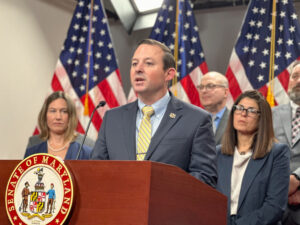 Photo showing a group of officials gathered at a podium with three United States flags behind them.